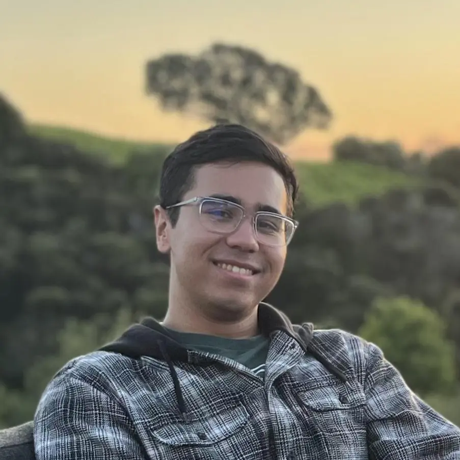 An image of Jacob Moy smiling behind a sunset and greenery.